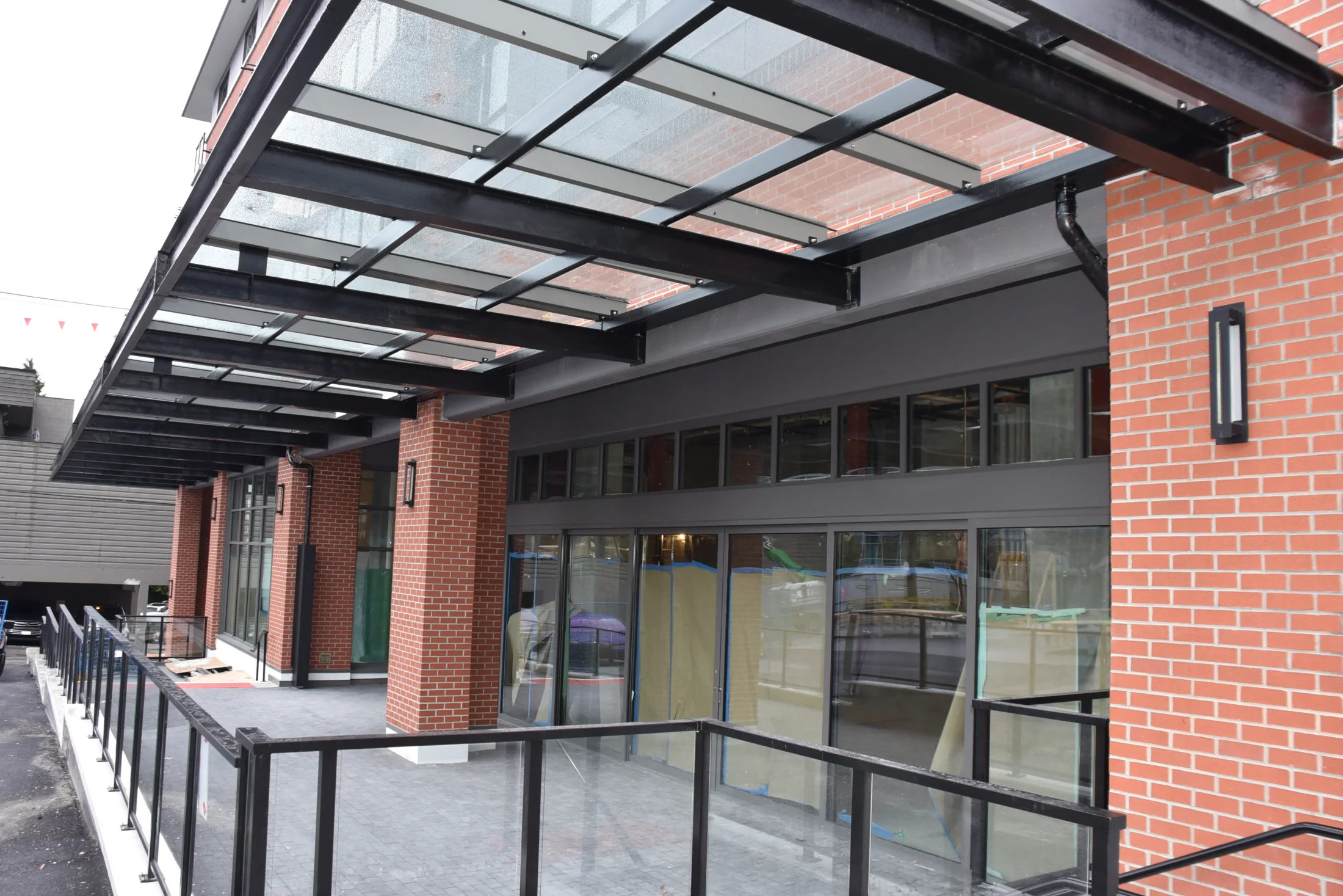 Vaha Overhead Glazing — Overhead glass panels bring daylight to a covered walkway beside a brick building.